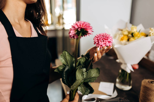 Florist in a pink t-shirt and black apron holds in her hands pink chrysanthemums - Photo, Image