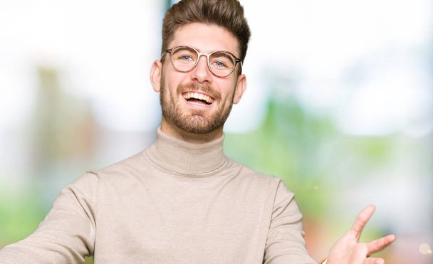 Mladý pohledný obchodní muž nosíš brýle při pohledu na fotoaparát s úsměvem otevřenou náručí objetí. Veselý výraz zahrnující štěstí. - Fotografie, Obrázek