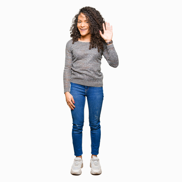 Young beautiful woman with curly hair wearing grey sweater Waiving saying hello happy and smiling, friendly welcome gesture - Fotoğraf, Görsel