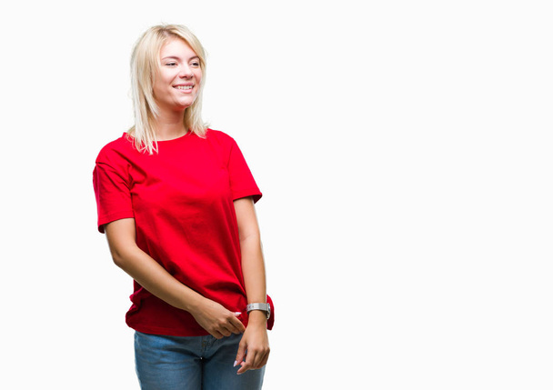 Fiatal gyönyörű szőke nő visel piros póló, felső elszigetelt háttér keres el az oldalon mosollyal arcán, természetes kifejezése. Nevetve magabiztos. - Fotó, kép