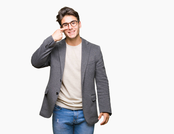 Young business man wearing glasses over isolated background Pointing with hand finger to face and nose, smiling cheerful - Foto, afbeelding