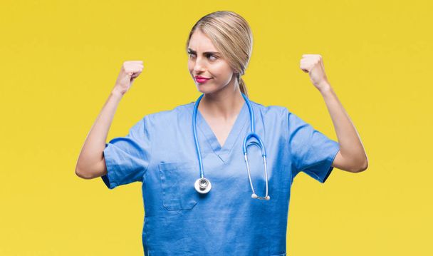 junge schöne blonde Ärztin Chirurgin Krankenschwester über isoliertem Hintergrund zeigt Armmuskeln lächeln stolz. Fitnesskonzept. - Foto, Bild
