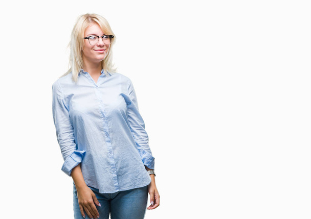 Young beautiful blonde business woman wearing glasses over isolated background looking away to side with smile on face, natural expression. Laughing confident. - Photo, Image