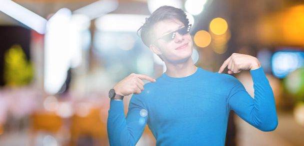 Young man wearing funny thug life glasses over isolated background looking confident with smile on face, pointing oneself with fingers proud and happy. - Photo, Image