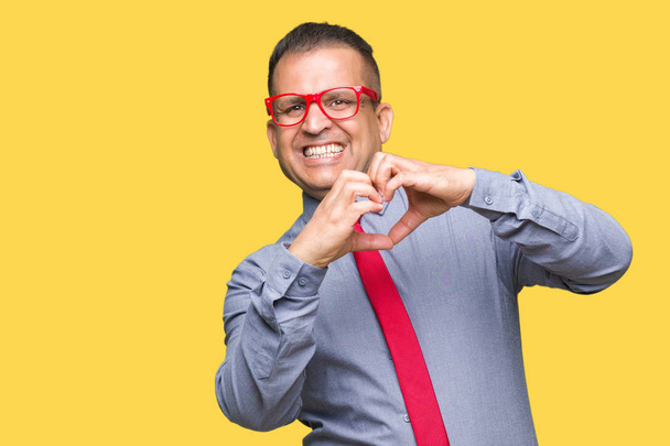 Арабський чоловік середнього віку носить модні червоні окуляри над ізольованим тлом, посміхаючись у коханні, демонструючи серцевий символ і форму руками. Романтична концепція
. - Фото, зображення