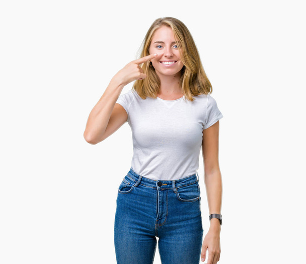 Mooie jonge vrouw dragen casual wit t-shirt over geïsoleerd background Pointing met hand vinger naar het gezicht en de neus, lacht vrolijk - Foto, afbeelding