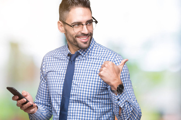 Człowiek młody biznes za pomocą smartfona na białym tle, wskazując i Wyświetlono z kciukiem do boku z szczęśliwy twarz uśmiechający się - Zdjęcie, obraz