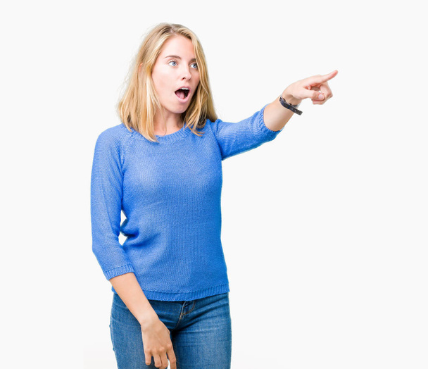 Beautiful young woman wearing blue sweater over isolated background Pointing with finger surprised ahead, open mouth amazed expression, something in front - Foto, immagini