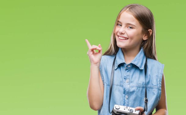 Menina bonita jovem tirar fotos usando a câmera vintage sobre fundo isolado muito feliz apontando com a mão e o dedo para o lado
 - Foto, Imagem
