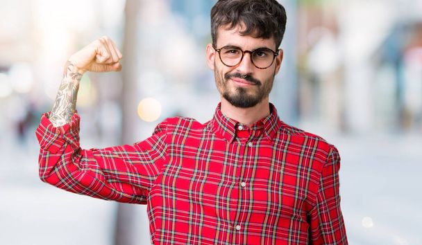 Joven hombre guapo con gafas sobre fondo aislado Persona fuerte que muestra el músculo del brazo, confiado y orgulloso de poder
 - Foto, imagen