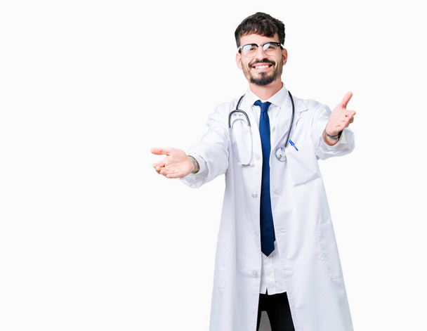 Fiatal orvos ember visel kabátot Kórház felett néz a kamerába, mosolyogva karokkal ölelés elszigetelt háttér. Vidám kifejezést átfogó boldogság. - Fotó, kép