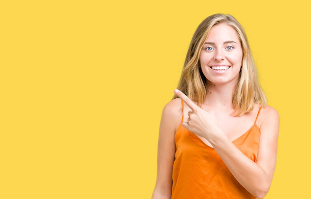 Όμορφη νεαρή γυναίκα που φοράει πορτοκαλί πουκάμισο πέρα από το απομονωμένο υπόβαθρο χαρούμενα με ένα χαμόγελο του προσώπου δείχνει με το χέρι και δάχτυλο μέχρι την πλευρά με ευτυχισμένο και φυσική έκφραση στο πρόσωπό - Φωτογραφία, εικόνα