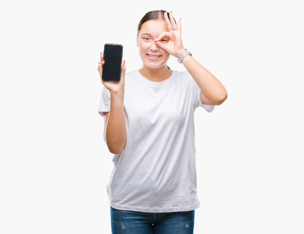 Joven hermosa mujer caucásica mostrando la pantalla del teléfono inteligente sobre un fondo aislado con la cara feliz sonriendo haciendo signo bien con la mano en el ojo mirando a través de los dedos
 - Foto, imagen