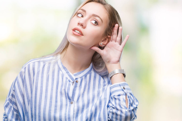 Young blonde woman over isolated background smiling with hand over ear listening an hearing to rumor or gossip. Deafness concept. - Foto, afbeelding