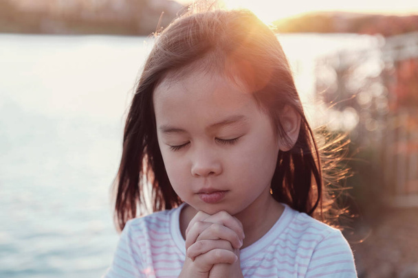 Multicultural little girl praying with sunflare background - Foto, Imagen