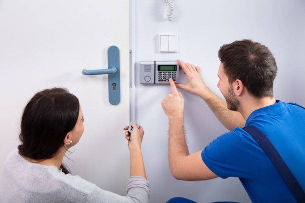 Close-up Of Handyman Installing Security System Near Door Wall While Woman Using Remote - Foto, imagen