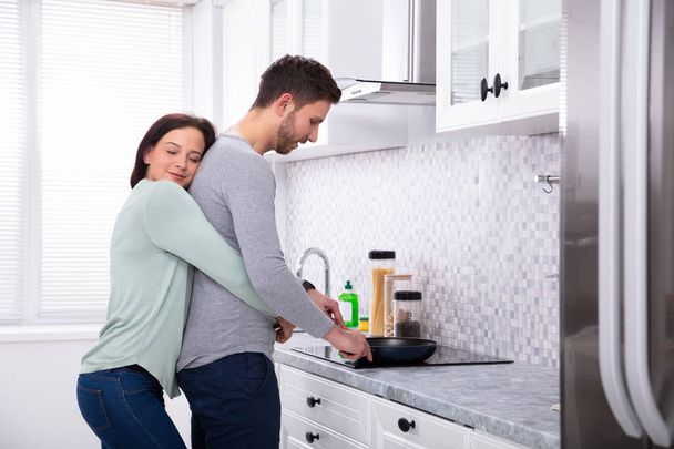 Junger Ehemann kocht Essen mit seiner lächelnden Ehefrau in der Küche - Foto, Bild