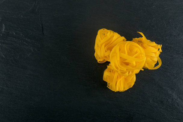 Raaka keltainen italialainen pasta fettuccine, fettuccelle tai tagliatelle lähikuva. Muna kotitekoinen kuiva nauha nuudelit, pitkä valssattu makaroni tai keittämätön spagetti musta kivi tausta ylhäältä
 - Valokuva, kuva