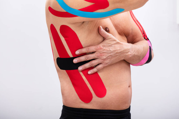 Homem aplicando vermelho e preto cinesiologia terapia torneira em suas costelas. A forma corporal estava alterada durante o retoque
 - Foto, Imagem