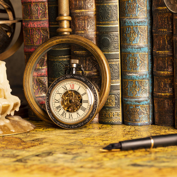 Antique clock on the background of a magnifying glass and books. Vintage style. 1565 old map of the year. - Fotografie, Obrázek