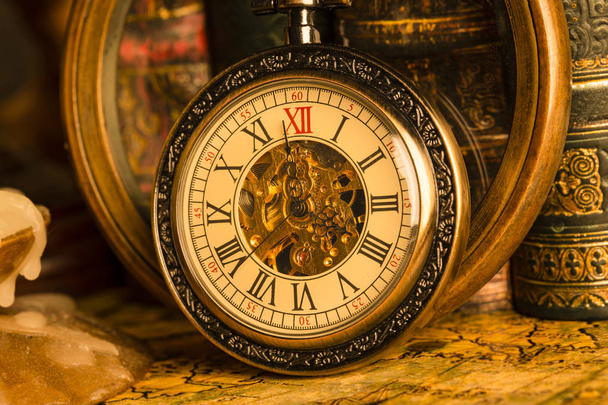 Antique clock on the background of a magnifying glass and books. Vintage style. 1565 old map of the year. - 写真・画像