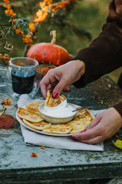 Autumn breakfast with pancakes. Cottage cheese pancakes ?ussian syrniki with sour cream. A woman in a brown sweater is drinking coffee. - Foto, afbeelding