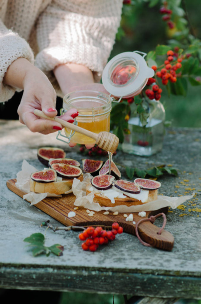 Women pours brusquets honey. Autumn sandwich with cheese, fresh figs, pine nuts and honey on rustic board - Photo, Image