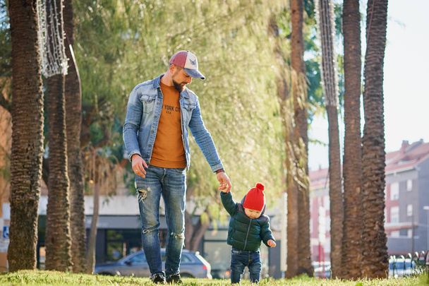 Cute happy little boy holding his father's hand when walking in the park on a sunny day. Father and son. - Foto, Bild