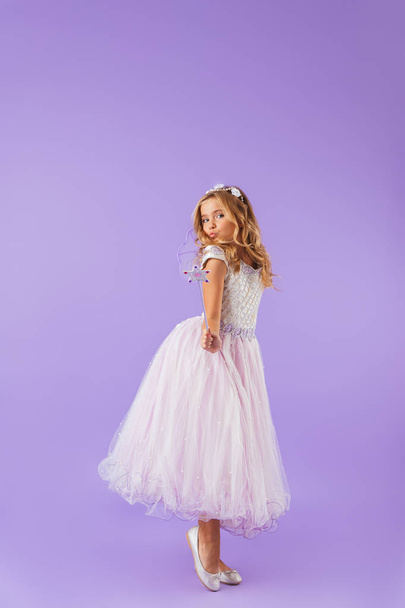 Full length portrait of a smiling pretty girl dressed in a princess dress isolated over violet background, holding magic wand - Foto, Bild