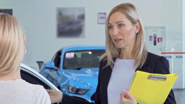 Зріла продавчиня розмовляє зі своїм клієнтом, працюючи в автосалоні
 - Кадри, відео