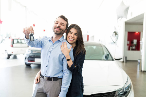 Portrait of happy and romantic mid adult couple with car keys in auto showroom - Фото, изображение