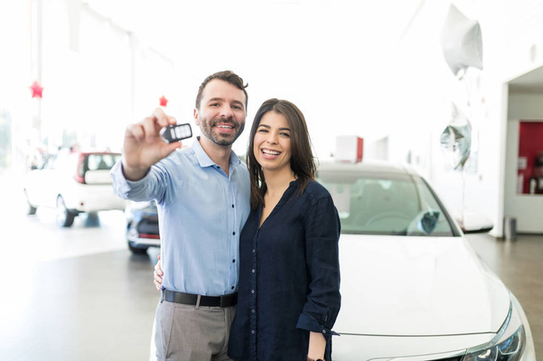 Wesoły łaciński mężczyzna i kobieta uśmiechając się pokazując nowe kluczyki do samochodu w salonie - Zdjęcie, obraz