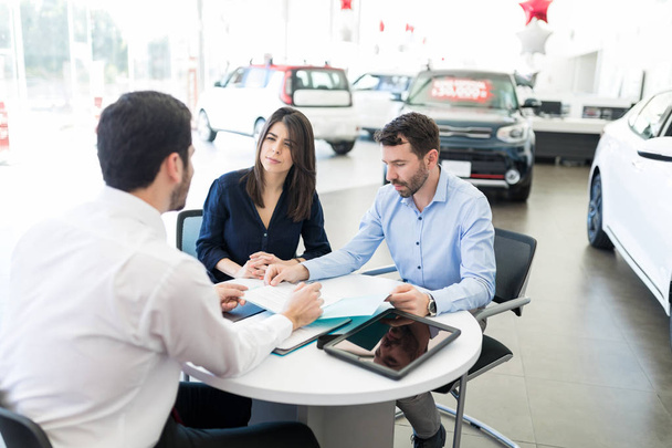 Latin man and woman going through terms and conditions carefully before buying car from showroom - Photo, Image