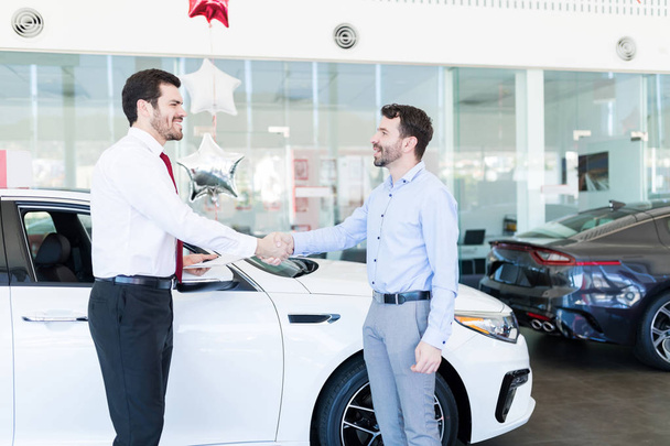 Красивый продавец встречает среднего взрослого мужчину на новой машине в выставочном зале
 - Фото, изображение