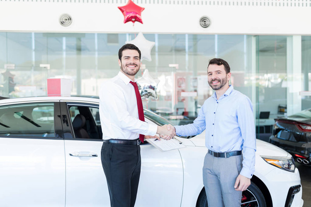 Portrait of smiling vehicle dealer and customer shaking hands in showroom - Photo, Image