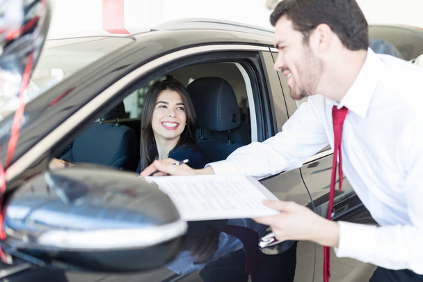 Salesman with financial document talking to client sitting in new car at showroom - Photo, image