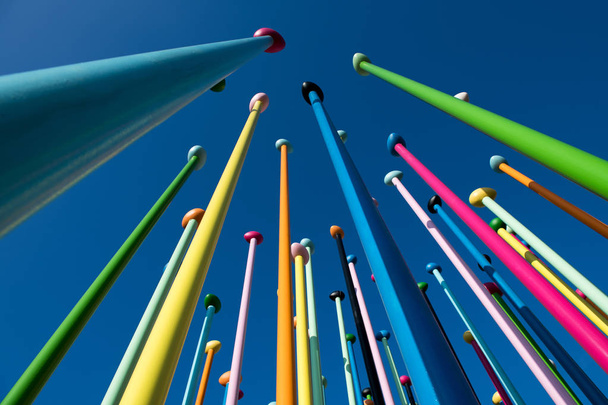 Nízký úhel barevné tenké Poláků proti modré obloze. Umělecké instalace. Koncept pozitivní a světlé pozadí - Fotografie, Obrázek