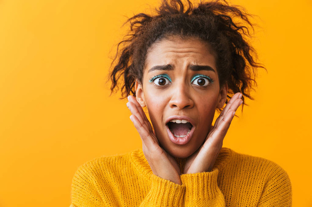 Shocked young african woman wearing sweater standing isolated over yellow background - Φωτογραφία, εικόνα