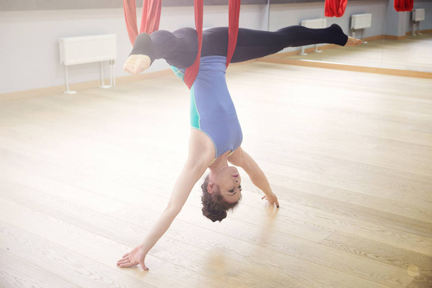 Adult woman practices aero anti-gravity yoga position in studio. Inversion bow pose in aero anti gravity yoga. Aerial exercises - Photo, Image