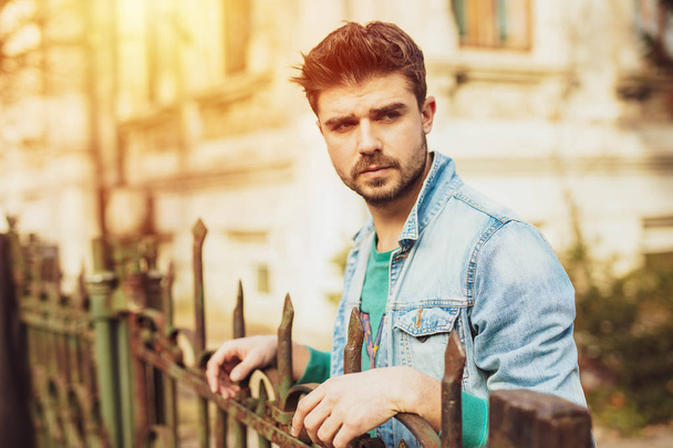 handsome guy in jeans jacket standing on a metal fence - Fotoğraf, Görsel