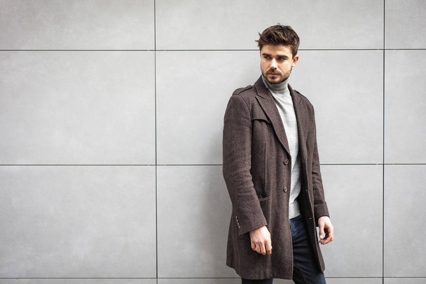 young attractive man in coat posing on a grey wall , stylish man - Фото, зображення
