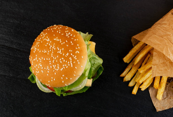 Burger fresco clássico com cebolas, verdes, queijo e batatas fritas enfeite vista superior. Hambúrguer ou frango em fundo de pedra preta natural
 - Foto, Imagem