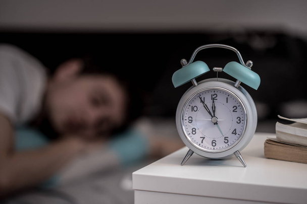 Fehér ébresztőóra az éjjeli szekrényre. Fiatal férfi alszik a háttérben.  - Fotó, kép
