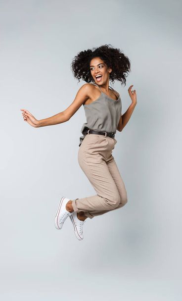 Full length of a happy young african woman casually dressed jumping isolated over gray background - Foto, afbeelding