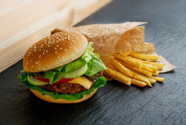 klassische frische Burger mit Zwiebeln, Gemüse, Käse und Pommes aus nächster Nähe garnieren. Hamburger oder Chickenburger auf schwarzem Natursteinhintergrund - Foto, Bild