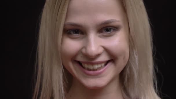 Ritratto ravvicinato di giovane ragazza caucasica dai capelli bianchi in maglione rosso che guarda sorridente nella fotocamera su sfondo nero
. - Filmati, video