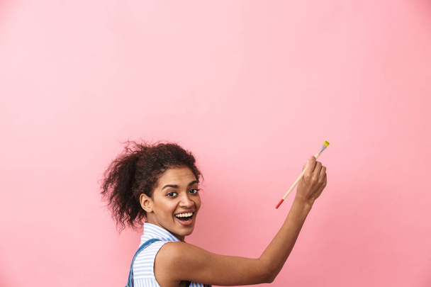 Beautiful young african woman atrist holding a paint brush over pink background - Foto, Imagem