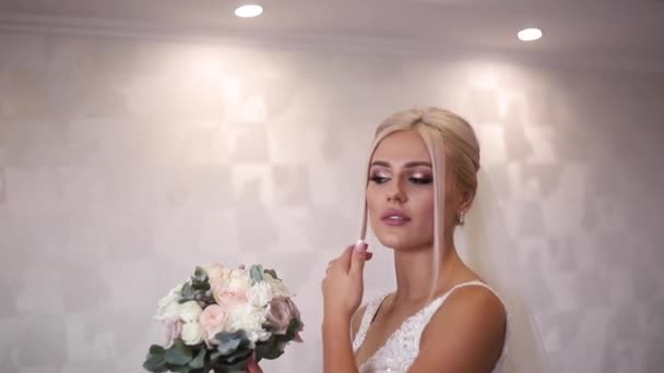 Elegantní nevěsta svatební kytici držet v rukou. Krásné blond vlasy dívka s módní make-up a účes. Model pro ženy v hotelu - Záběry, video