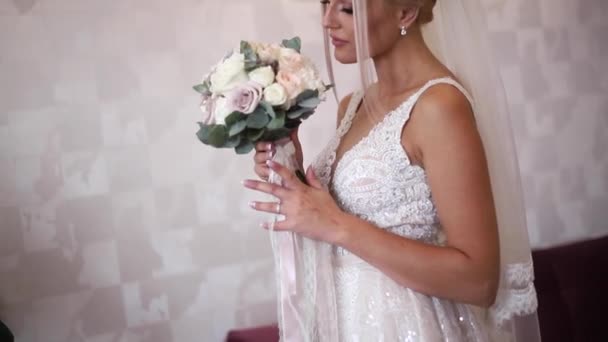 Элегантная невеста держит свадебный букет в руках. Девушка с модным макияжем и прической. Женская модель в отеле
. - Кадры, видео