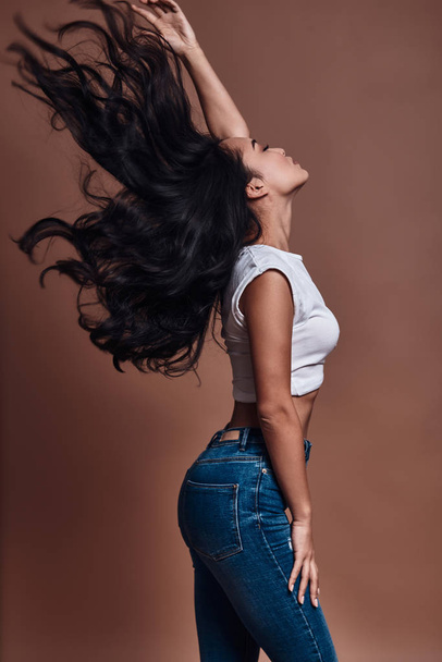 Strong hair, Beautiful young woman touching her hair while standing against brown background - Foto, Imagem